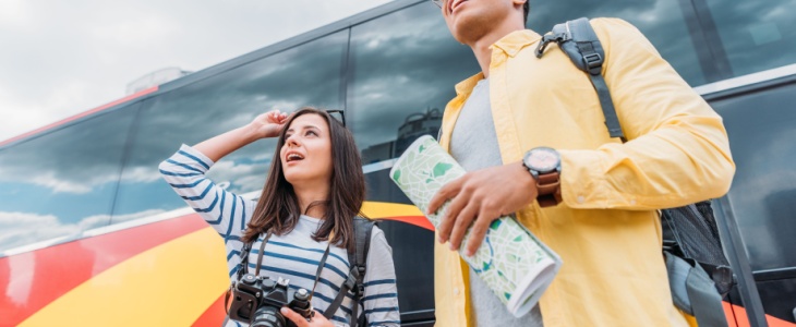 a man and woman look around excitedly outside their tour bus