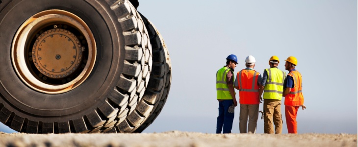 a large truck is next to the camera while four workers stand talking in the foreground